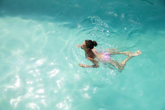 Biracial woman spending time at home self isolating and social distancing in quarantine lockdown during coronavirus covid 19 epidemic, swimming in the swimming pool.