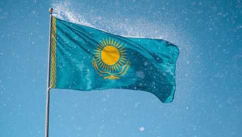 Waving Kazakhstan flag with golden sun and eagle against sparkling blue sky