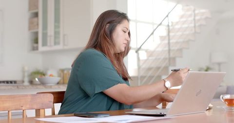Dedicated Woman Working From Home at Dining Table with Laptop
