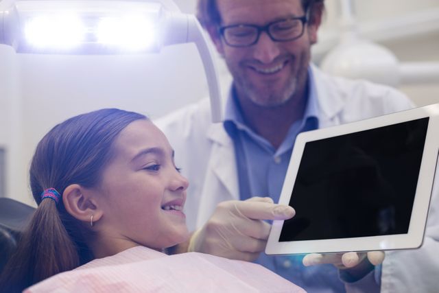Dentist demonstrating dental information on a digital tablet to a young patient in a dental clinic. Useful for illustrating modern dental practices, pediatric dentistry, patient education, and the use of technology in healthcare.