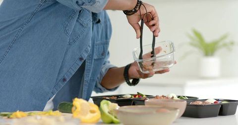 Man preparing healthy meals, filling meal-prep trays in bright minimalist home kitchen