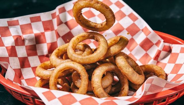 Tumbling golden onion rings in red basket on checkered liner for diner menus and ads