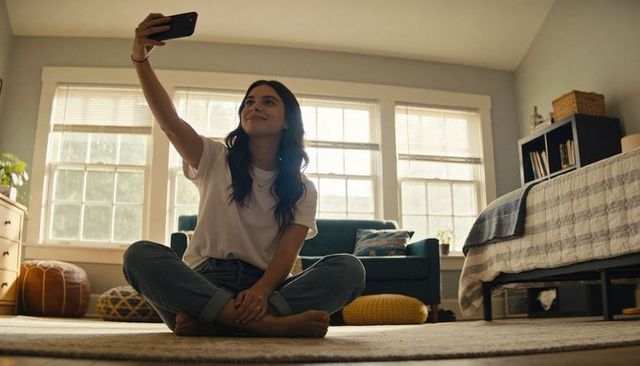 Young woman taking selfie while sitting cross-legged on cozy bedroom rug
