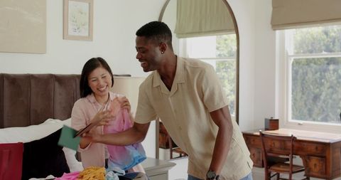 Diverse Couple Joyfully Packing Colorful Clothes in Bedroom