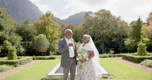 Happy diverse senior bride and groom drinking champagne at their wedding in sunny garden, copy space. Summer, marriage, romance, love, celebration, tradition and senior lifestyle, unaltered.