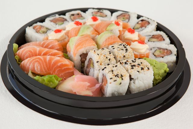 Set of assorted sushi kept in a round black box against white background