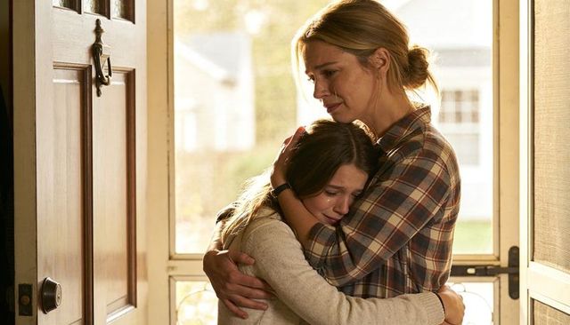 Comforting mother embracing crying teenage daughter in sunlit doorway, tender family moment