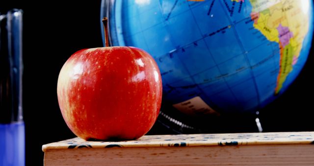 A red apple sits prominently on a wooden surface in front of a colorful globe, with copy space. Symbolizing education and learning, the apple and globe are classic icons of knowledge and global awareness.