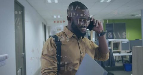 Smiling professional walking through office talking on phone carrying laptop with code overlay