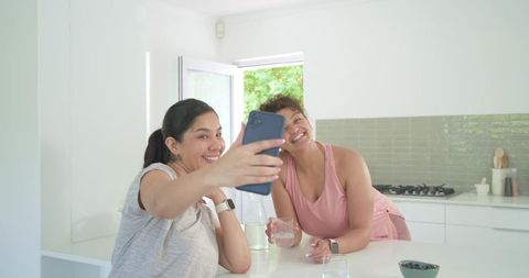 Friends taking selfie at bright modern kitchen island, laughing casual home lifestyle