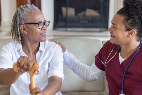 Senior woman sitting with cane receiving compassionate in-home care, nurse offering support