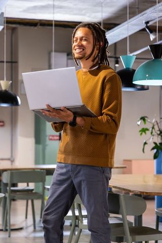 Smiling African American man holding laptop and working in bright modern coworking space