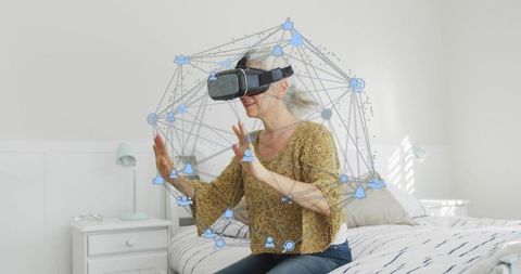 Senior woman exploring virtual reality network in minimalist bedroom with vr headset