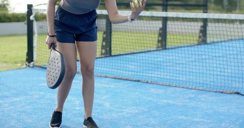 African american woman preparing serve with paddle and ball on blue outdoor padel court
