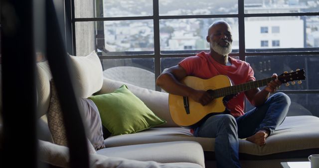 Relaxed Senior Man Playing Acoustic Guitar on Couch Near Window - Download Free Stock Images Pikwizard.com