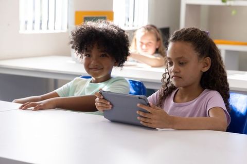 Diverse students using tablet for learning together in bright classroom