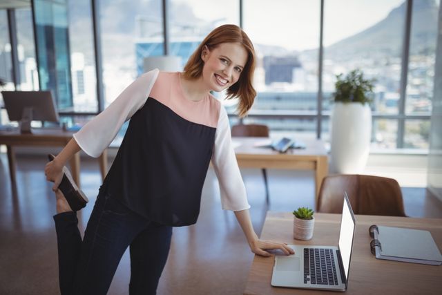 Smiling executive stretching while working in a modern office. Ideal for illustrating concepts of work-life balance, healthy workplace habits, and productivity. Useful for corporate wellness programs, business articles, and office environment promotions.