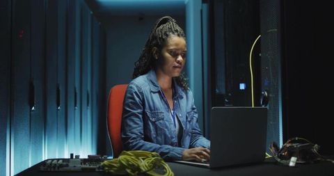 It technician working on laptop in server room with ethernet cables and blue lighting