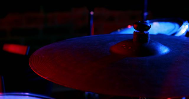 Close-up view of cymbal captured under dramatic blue and red lighting, creating a moody atmosphere during a live concert. Ideal for use in music-related publications, concert promotions, advertisements for musical instruments, or as a background image for music blogs and websites highlighting live performances or drum-focused content.
