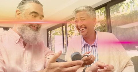 Mature couple checking blood pressure at home, laughing during wellness routine