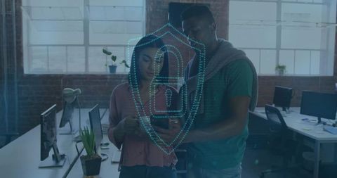 Young professionals collaborating on mobile cybersecurity in loft office with digital shield