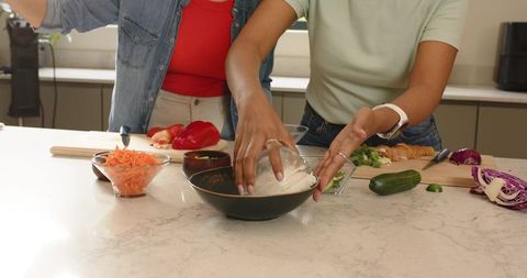 Diverse women pouring rice and chopping vegetables on kitchen island