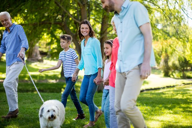 Family enjoying a sunny day in the park, walking their dog and spending quality time together. Ideal for use in advertisements, family-oriented campaigns, lifestyle blogs, and articles about family bonding, outdoor activities, and pet ownership.