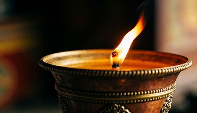 Antique bronze oil lamp burning, flickering flame, ornate beaded motifs, close-up