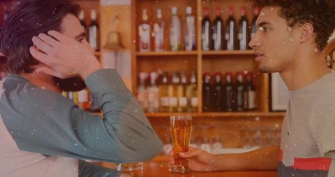 Two men leaning at bar counter holding beer pints talking over drinks warm wood interior