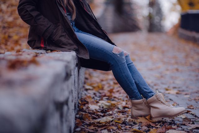 Young Woman Sitting Outdoors in Autumn Wearing Ripped Jeans and Beige Boots - Download Free Stock Photos Pikwizard.com