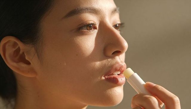 Asian woman applying lip balm closeup showing dewy skin natural makeup and lip care