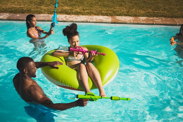 Group of friends having fun in a swimming pool, playing with water pistols. Ideal for use in advertisements, social media posts, and articles related to summer activities, outdoor fun, and leisure time. Perfect for promoting pool parties, summer vacations, and water toys.