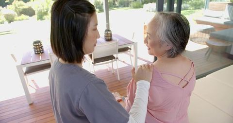 Caregiver gently comforting senior woman on sunlit patio deck, family support moment
