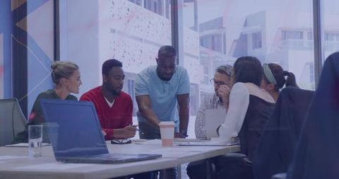Diverse team collaborating around table reviewing laptop and documents in bright office