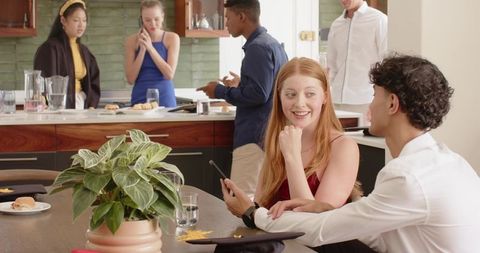 Graduation hangout at-home kitchen party with friends chatting, laughing and using phones