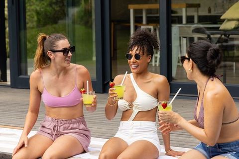Friends enjoying summer cocktails on deck in swimwear and sunglasses, candid laughter