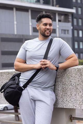 African american commuter leaning on overpass in gray activewear with black duffel, urban lifestyle