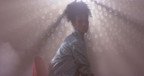 Moody cinematic woman sitting in haze wearing satin jacket with dotted light beams