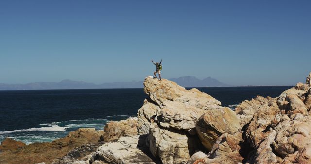 African american man hiking raising hands standing on rock by the sea. fitness training and healthy outdoor lifestyle.