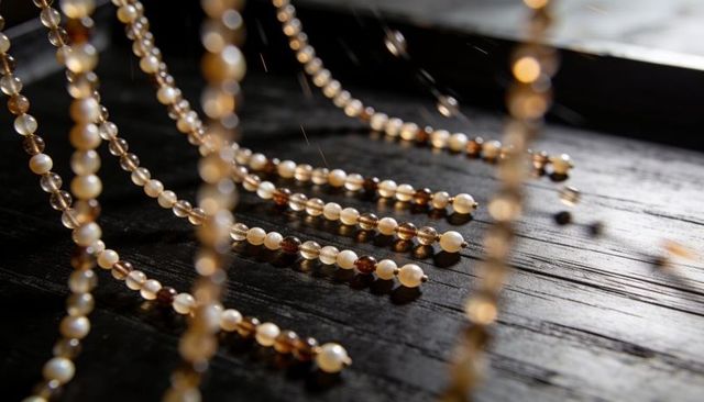 Hanging pearl and amber bead strands gleaming and casting shadows on dark wooden tabletop