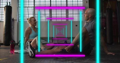 Sitting gym partners stretching and chatting amid neon tunnel glow in urban fitness studio