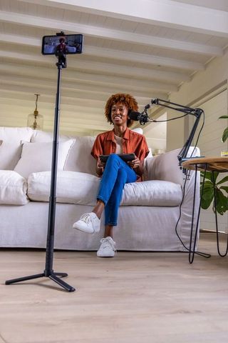African american creator livestreaming from home studio on sofa with tablet and boom mic