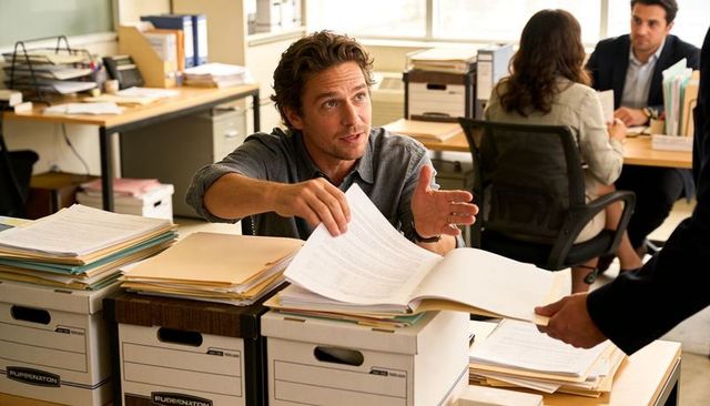 Male employee handing paperwork in busy open-plan office with archive boxes and files