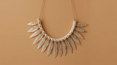 Elegant metallic feather necklace with gemstones on tan background