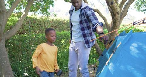 African american father and son adjusting blue tent poles during backyard camping