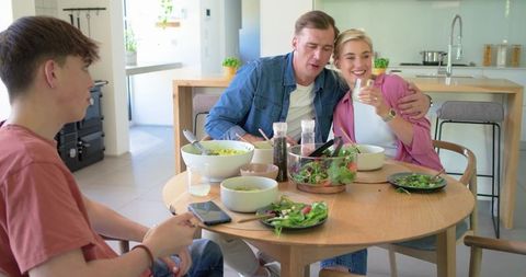 Modern family sharing healthy salad around round wooden table during casual mealtime