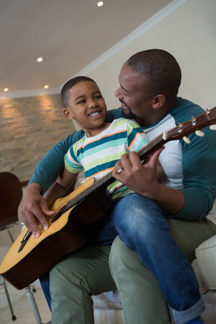 Father teaching his son to play the guitar in living room