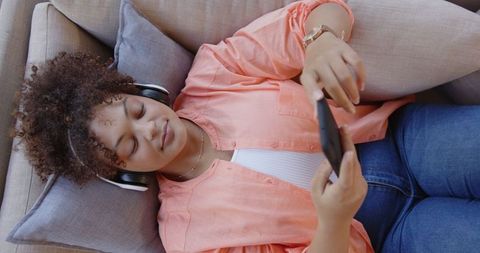 African american woman relaxing with headphones and smartphone on sofa