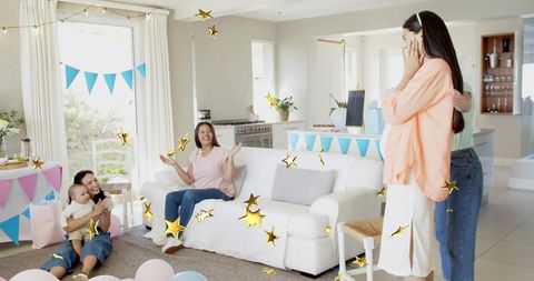 Pregnant woman covering face and receiving hug during pastel baby shower party at home