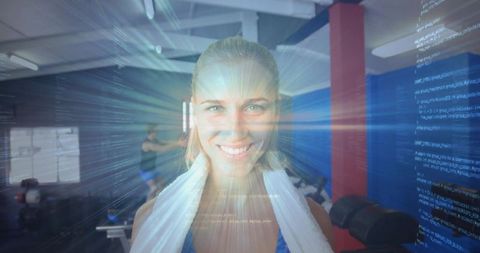 Smiling woman radiating energy with holographic code overlay with white towel standing in gym